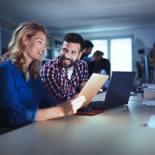 Smiling colleagues discussing a project on a tablet in a bright office, representing GAIA Code AI's contact and support team